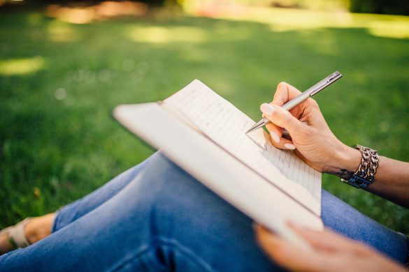 Woman writing in a journal sitting on grass.